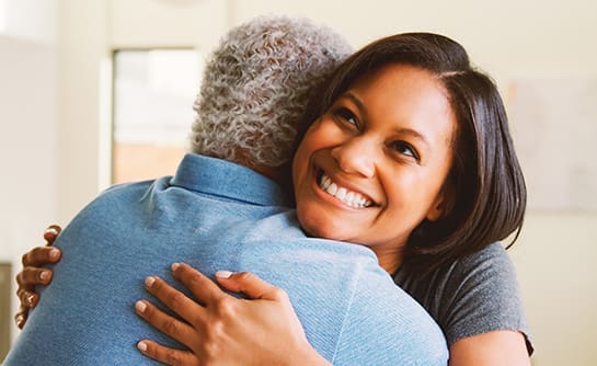 Senior Father Being Hugged By Smiling Adult Daughter At Home