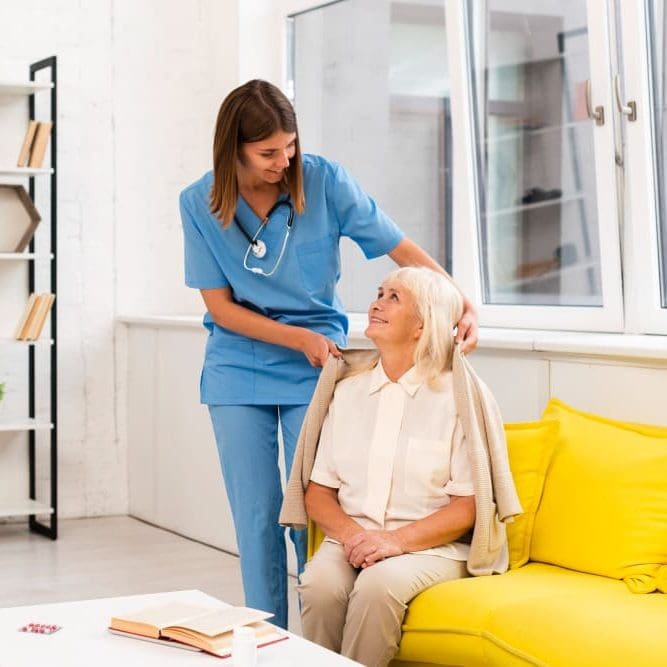 A caregiver putting a sweater on a woman's shoulders.